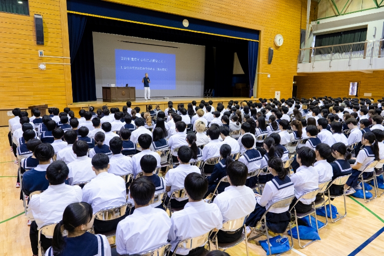 学校の講堂の舞台で平井さんが講演している写真