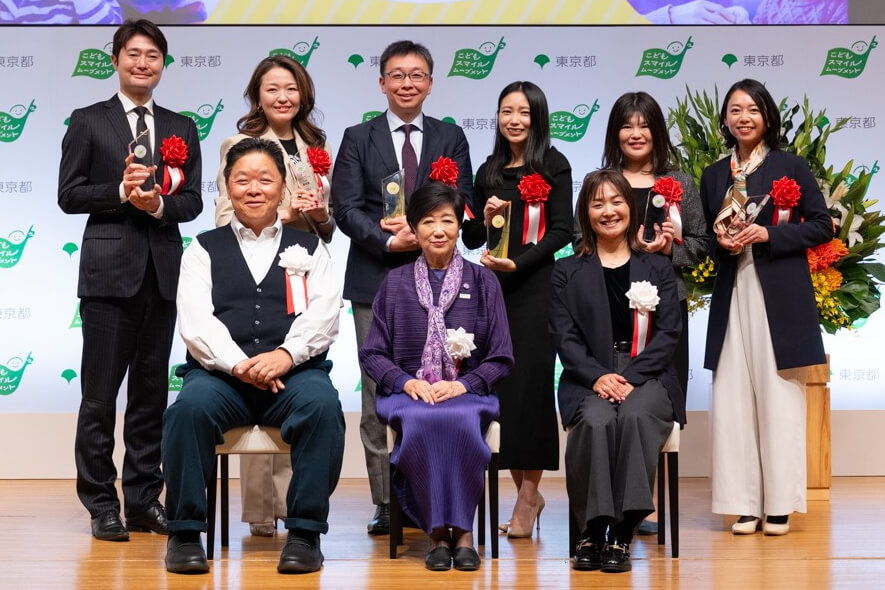 小池百合子都知事、こどもスマイルムーブメントアンバサダーの伊集院 光さん、パラアスリートの谷 真海さん、こどもスマイルムーブメント大賞を受賞した各団体の代表者が並んで登壇している様子