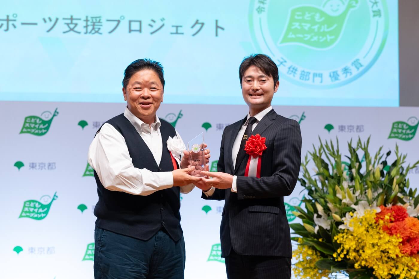 株式会社biimaの代表者がこどもスマイルムーブメントアンバサダーの伊集院光さんから優秀賞の盾を受け取っている様子