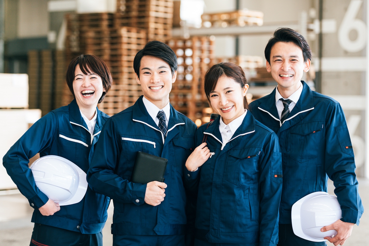 作業着を着た4人が笑顔で並んでいる写真